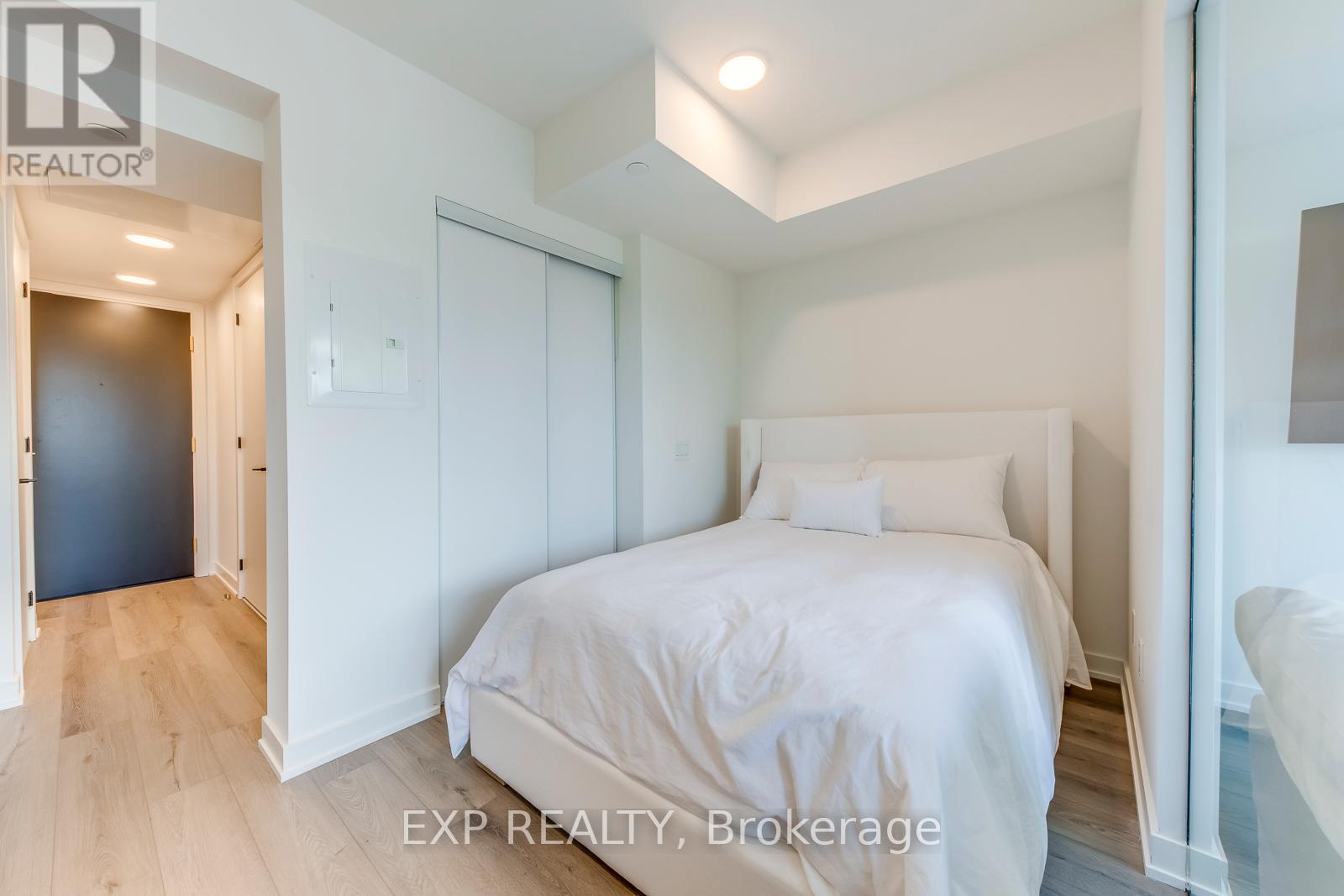 A bedroom with a bed, a nightstand, and a door leading to another room.