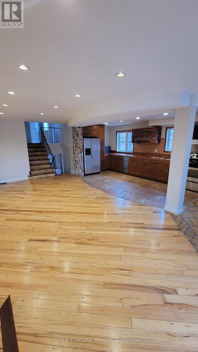 A spacious room with wooden flooring and a staircase.