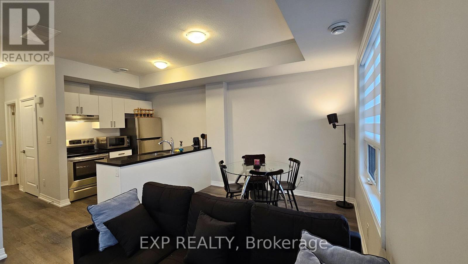 A well-lit kitchen and dining area with a black sofa and chairs.