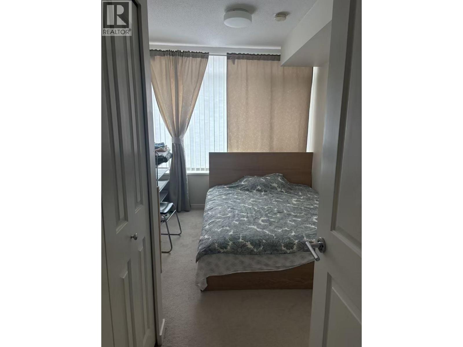 A bedroom with a bed, chair, and window with curtains.