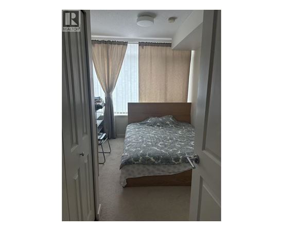 A bedroom with a bed, chair, and window with curtains.