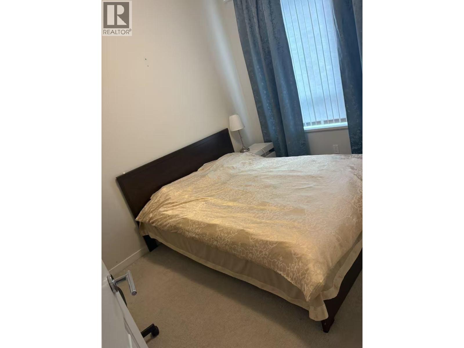 A bed with a white sheet and a pillow is in the corner of a room with a window.