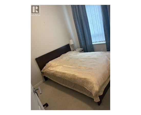 A bed with a white sheet and a pillow is in the corner of a room with a window.