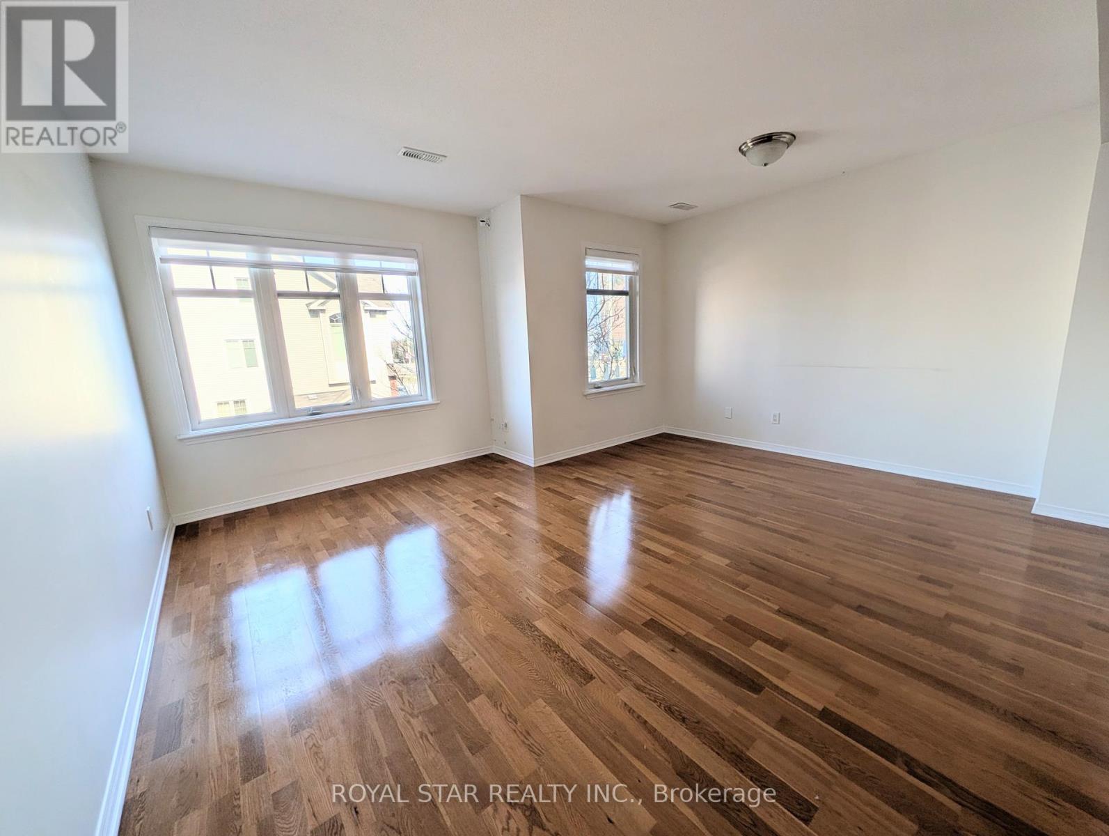 A spacious room with wooden flooring and two windows.
