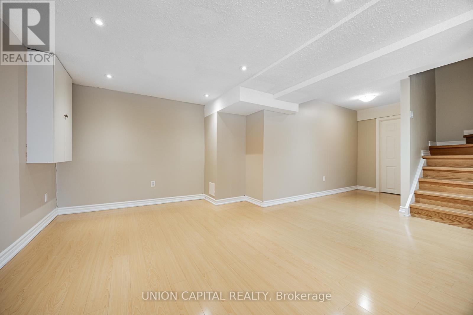 A spacious room with wooden flooring and beige walls, with a staircase on the right side.