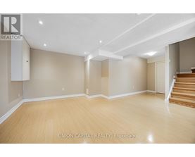 A spacious room with wooden flooring and beige walls, with a staircase on the right side.