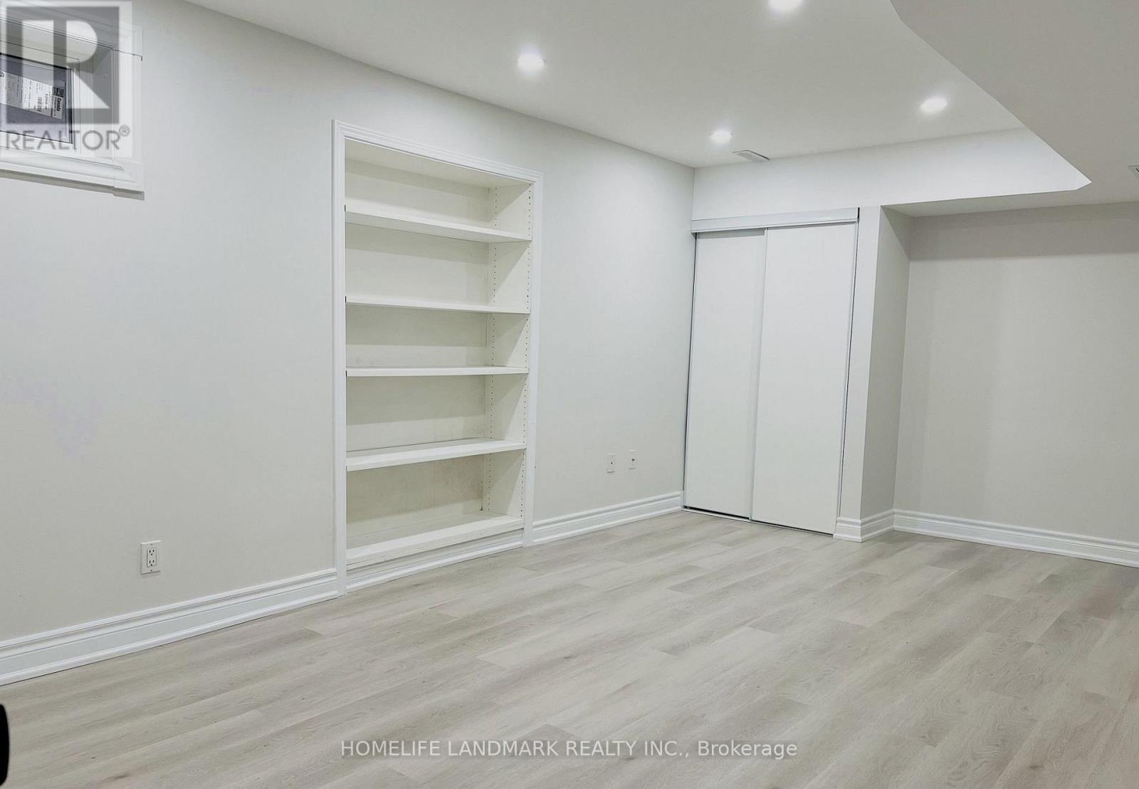 A room with white walls and wooden flooring, with a sign that reads "REALTOR" on the wall.