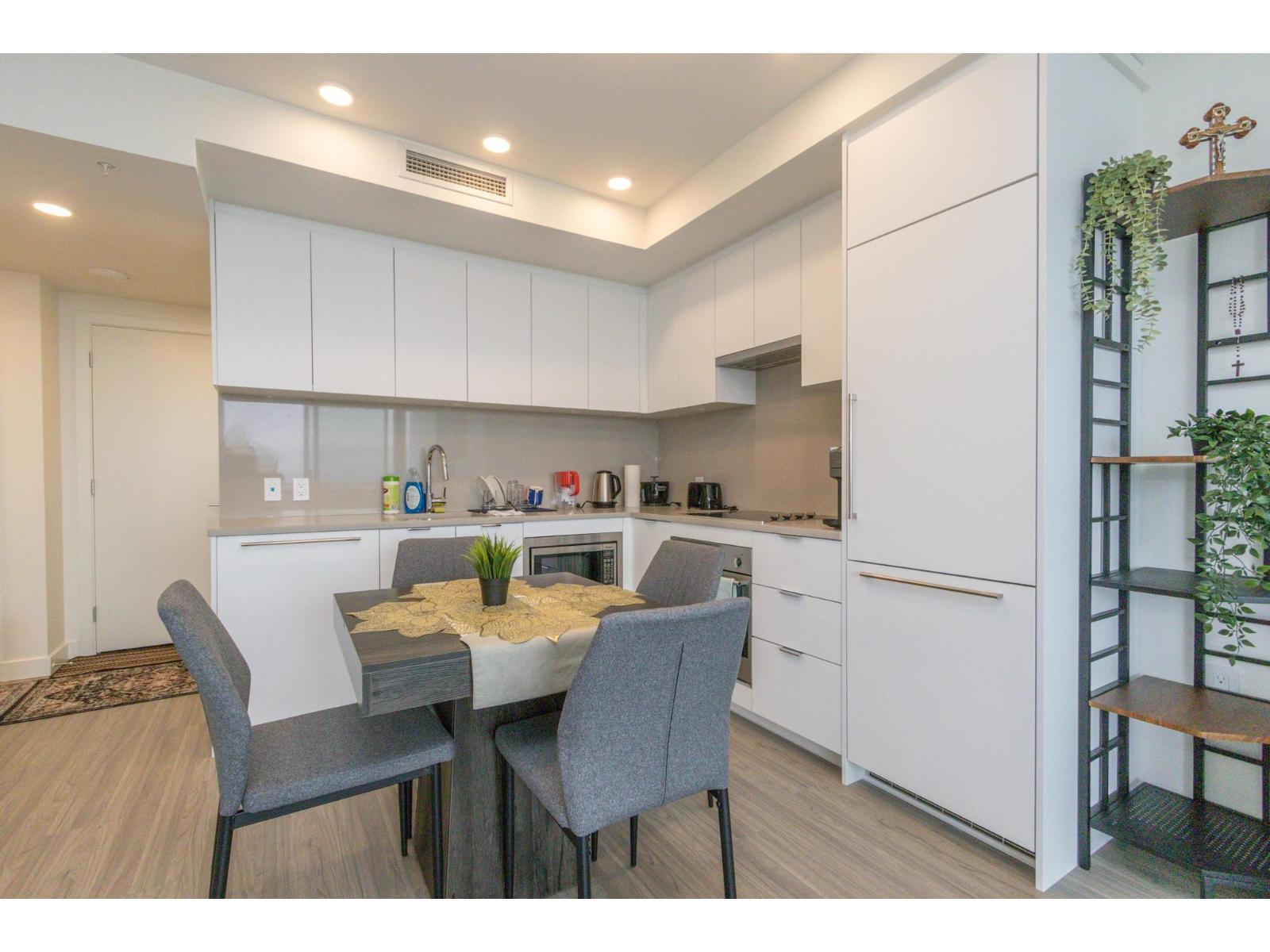 A kitchen with a table and chairs in the foreground and a shelf with plants on it in the background.