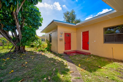 A small house with a red door is surrounded by greenery.