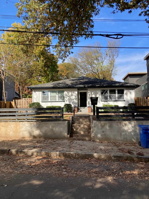 A small house with a black roof and a white door is surrounded by a wooden fence.