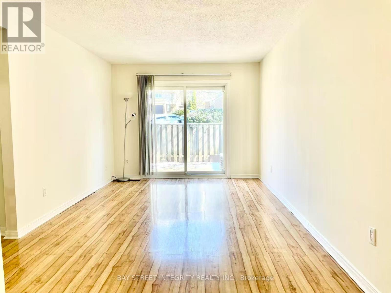 A spacious room with wooden floors and a sliding glass door leading outside.