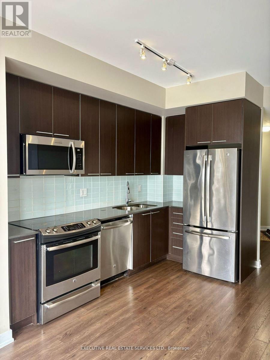 A modern kitchen with dark wood cabinets and stainless steel appliances.