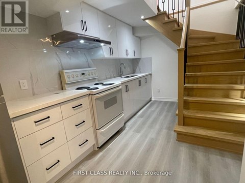A modern kitchen with a stainless steel oven and wooden staircase.
