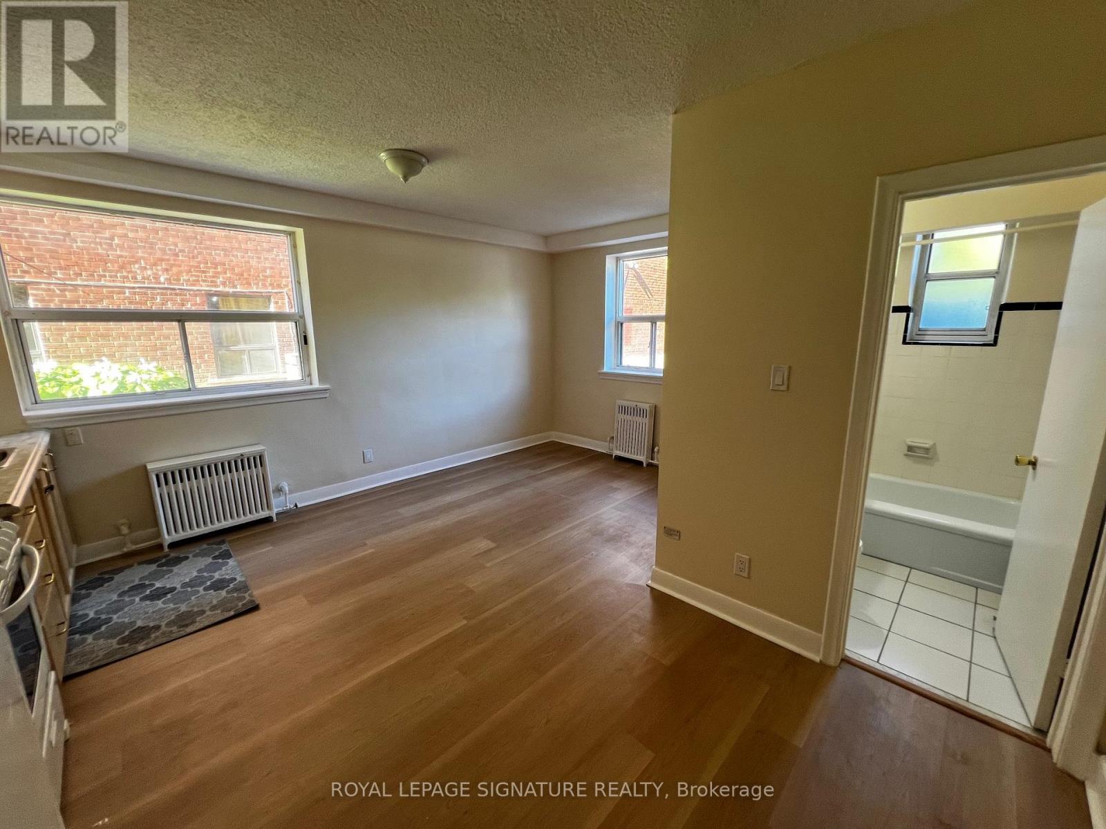 A room with wooden floors and a window with a view of a brick building outside.