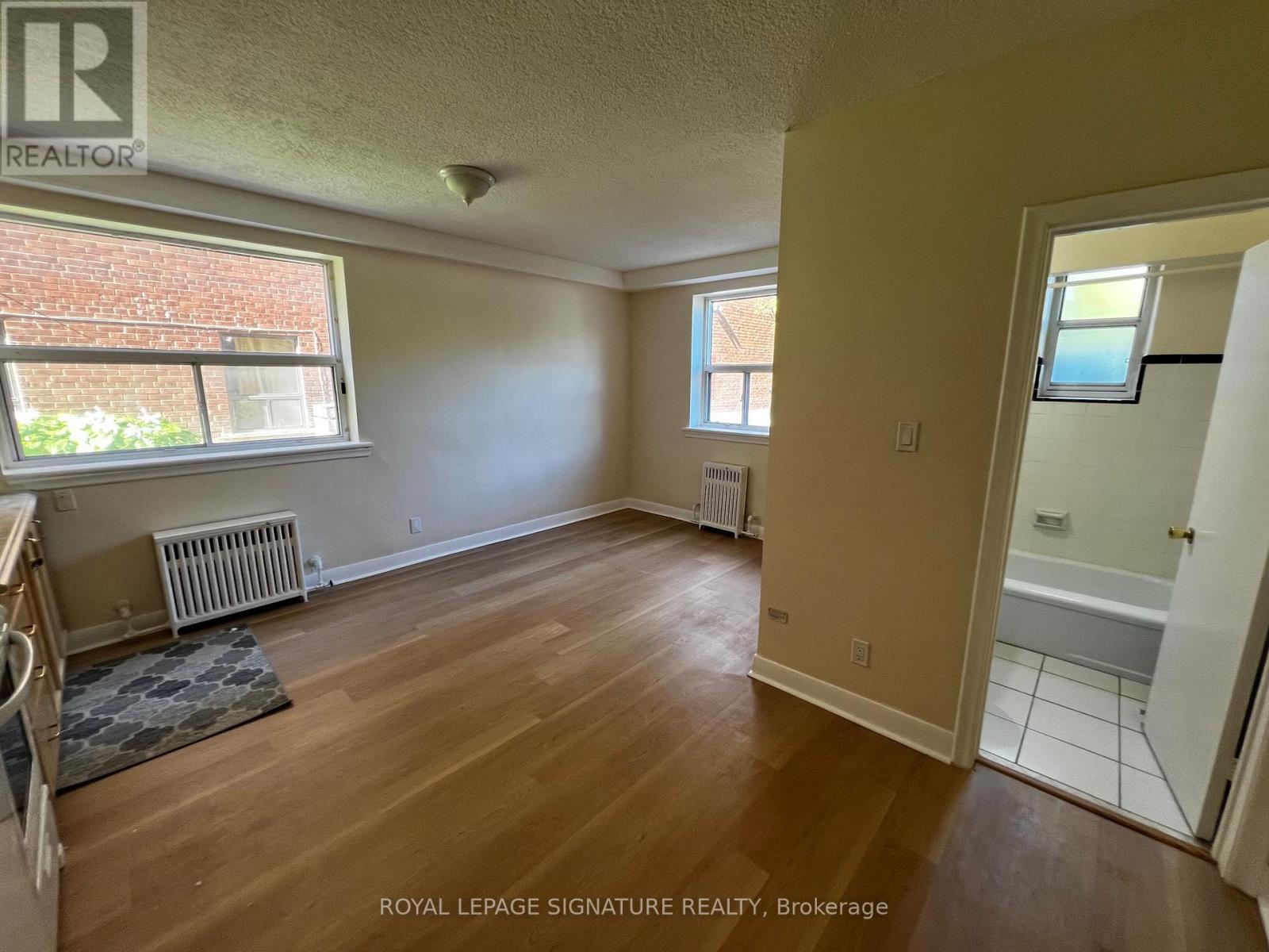 A room with wooden floors and a window with a view of a brick building.