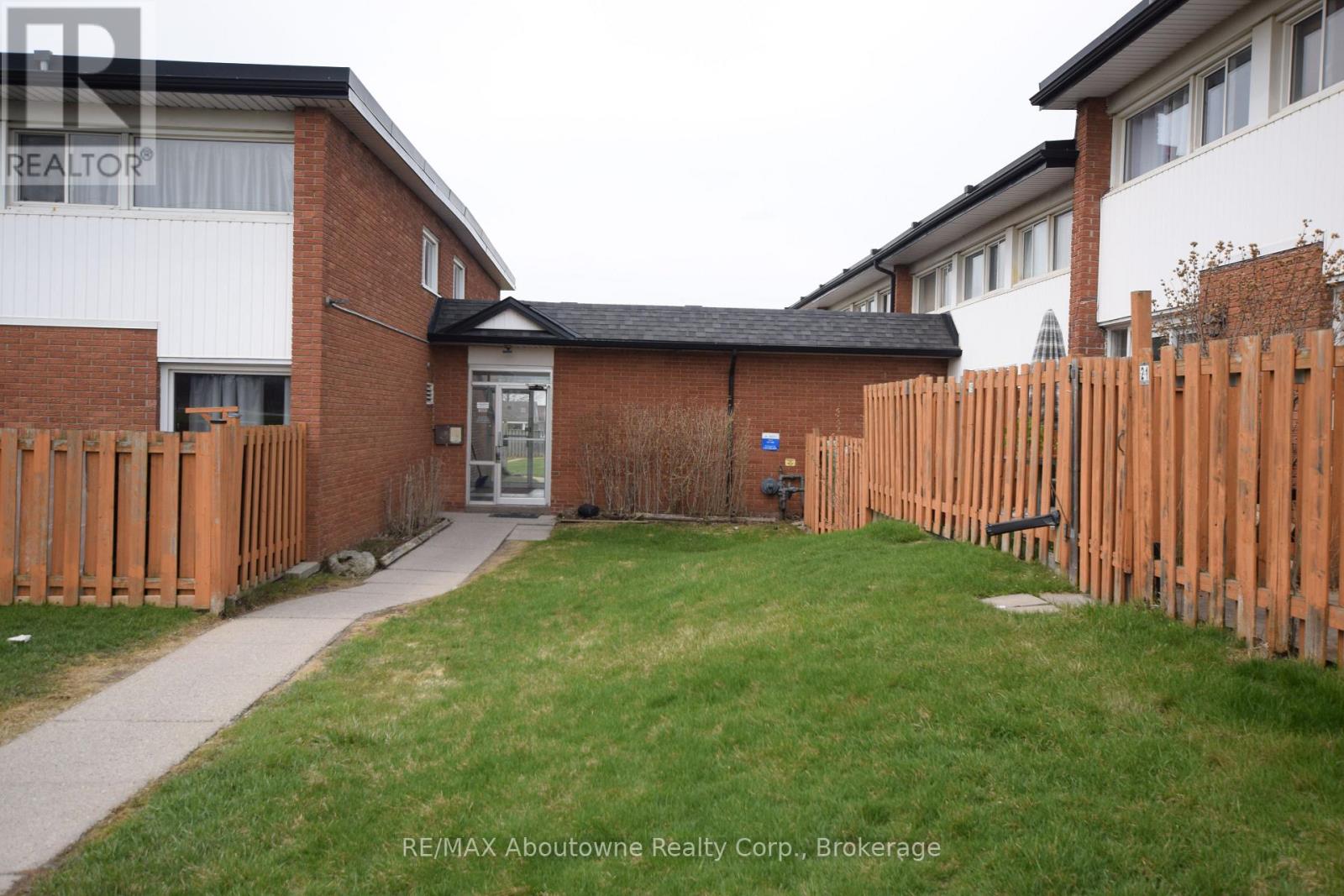 A small grassy yard with a wooden fence and a brick building in the background.