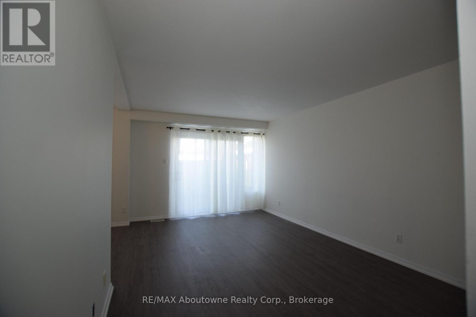 A large empty room with a window covered in white curtains.
