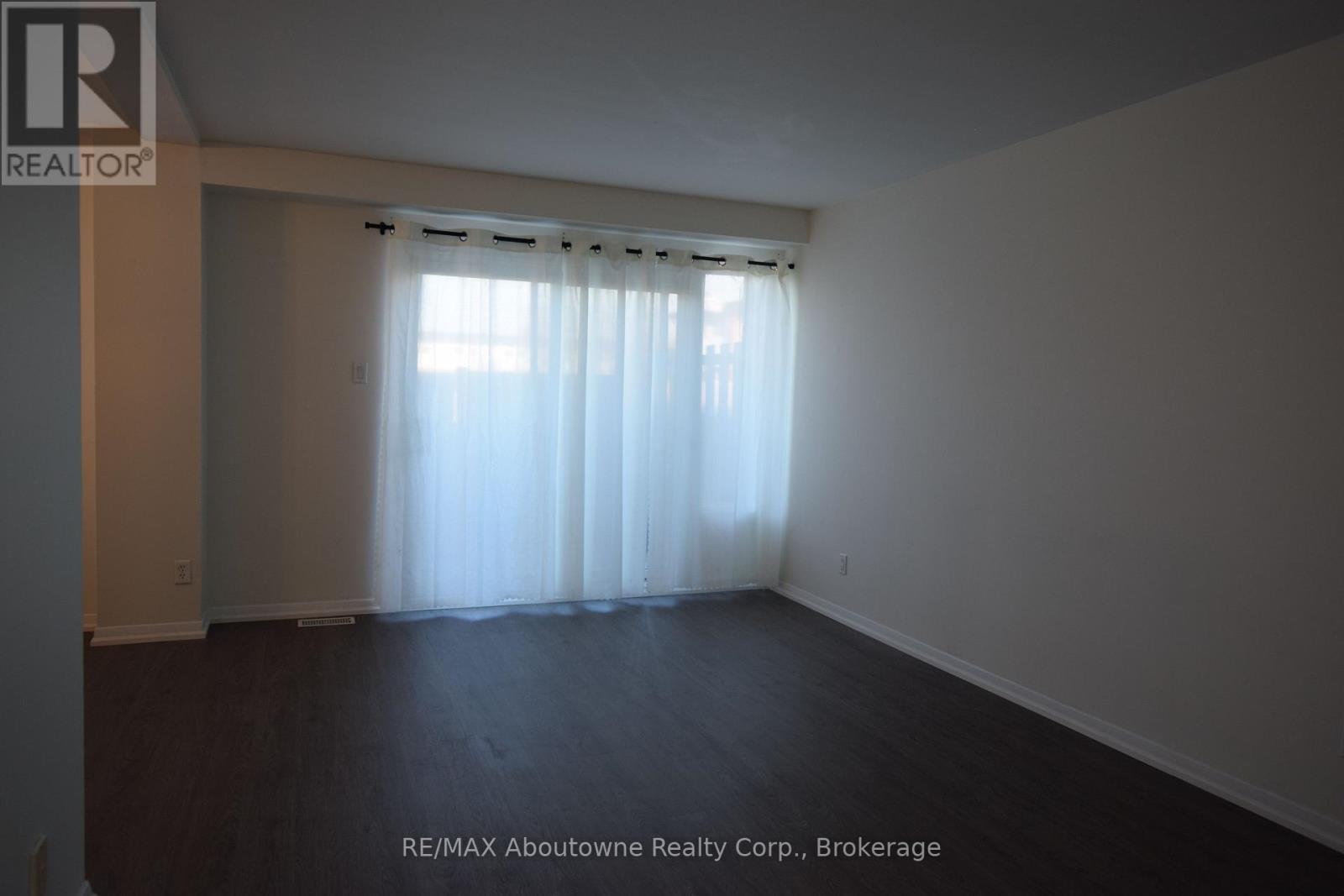 A large empty room with a window covered by sheer curtains.