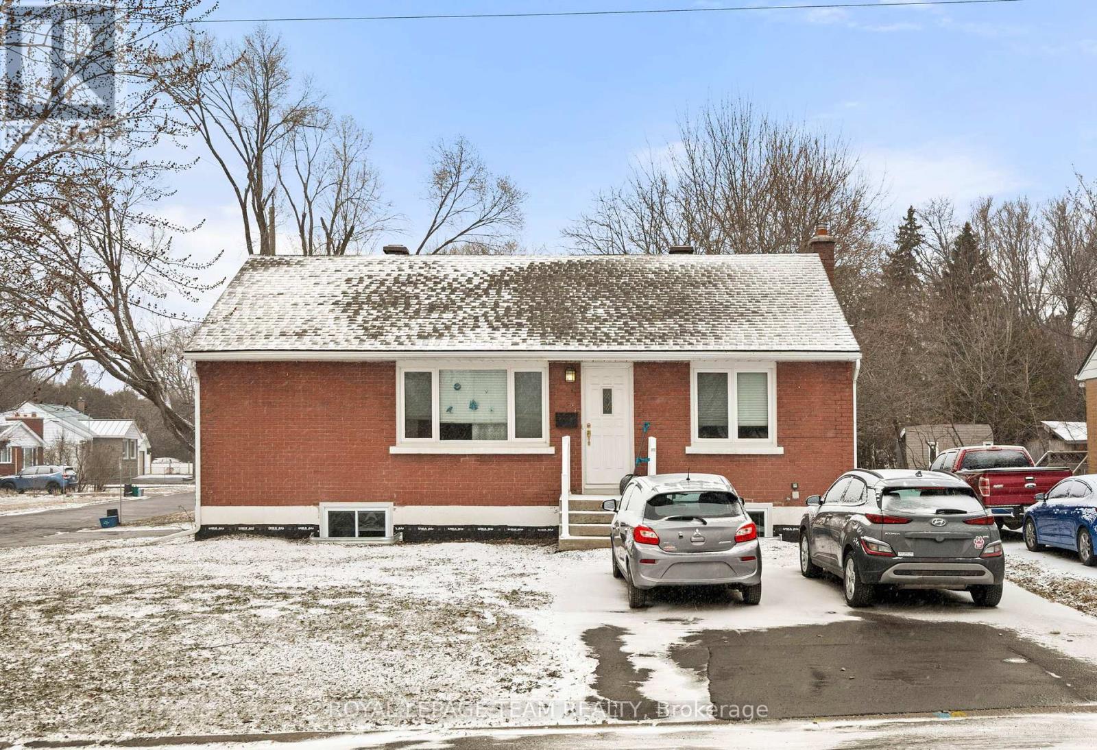 A red brick house with a white door and windows, surrounded by parked cars.