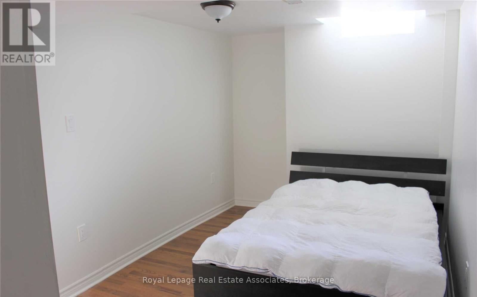 A bedroom with a bed, wooden floor, and white walls.
