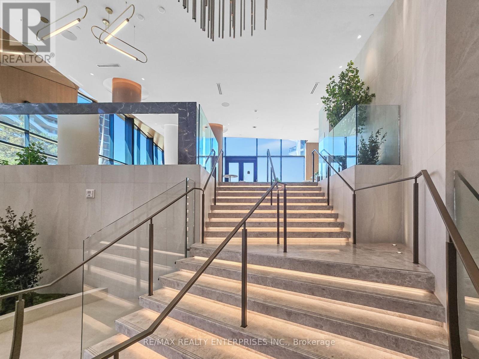 A staircase with glass railings leads to a brightly lit open space.