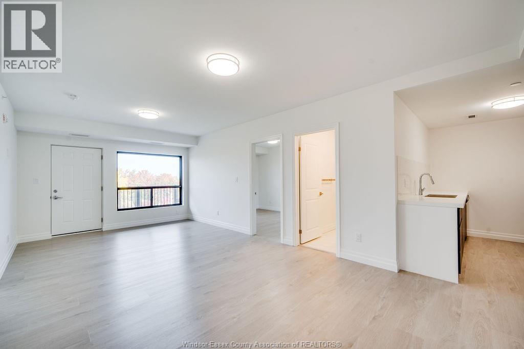 A spacious, empty room with a kitchenette and a balcony.