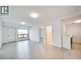 A spacious, empty room with a kitchenette and a balcony.