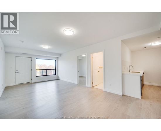 A spacious, empty room with a kitchenette and a balcony.