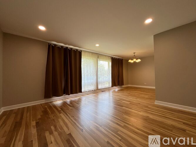 A spacious room with wooden flooring and a large window with curtains.