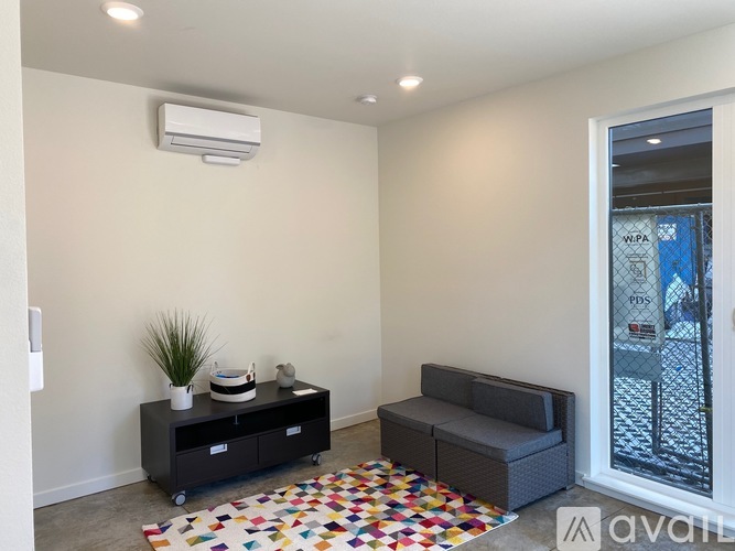 A room with a black sofa, a plant, and a white air conditioner unit.