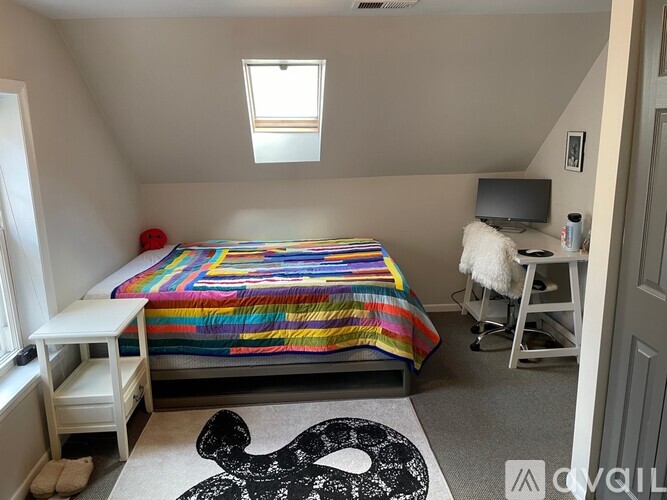 A bedroom with a bed, a chair, and a rug with a black design on it.