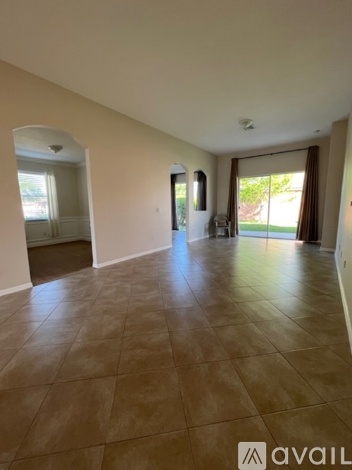 A spacious room with tiled flooring and a sliding glass door leading to a garden.