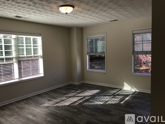 A room with a window on the left and a window on the right with a view of trees outside.