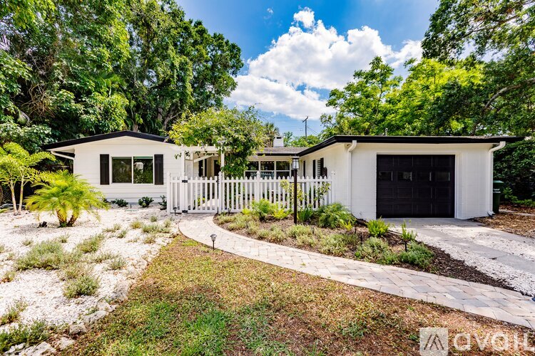 A white house with a black garage door is surrounded by greenery.
