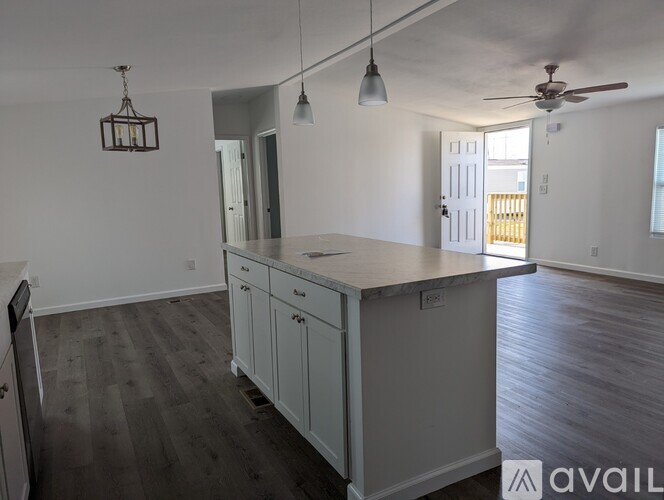 A kitchen with a white countertop and cabinets, a ceiling fan, and pendant lights.