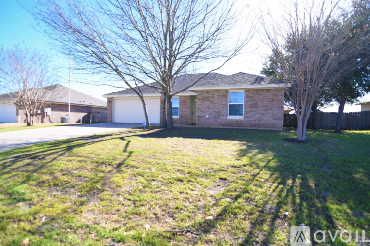 A house with a brown brick exterior and a white garage door is surrounded by a grassy lawn and leafless trees.