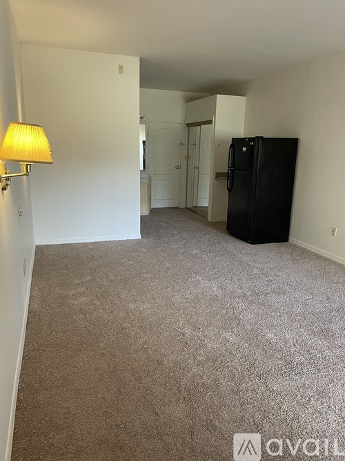 A room with a black fridge and a yellow lamp.
