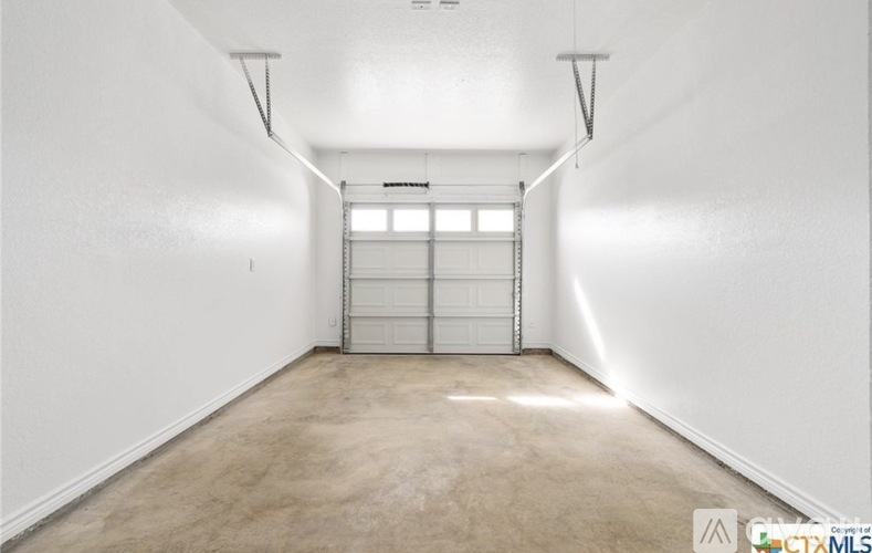 A spacious room with a white door and lighting fixtures on the ceiling.