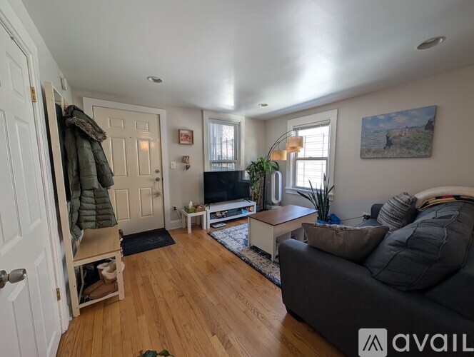 A living room with a grey couch, a wooden floor, and a painting on the wall.