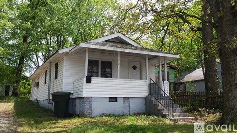 A small white house with a black trash bin in front of it.