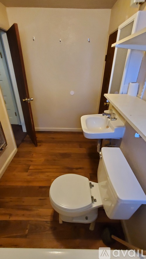 A white toilet sits in a bathroom with wood floors and white walls.
