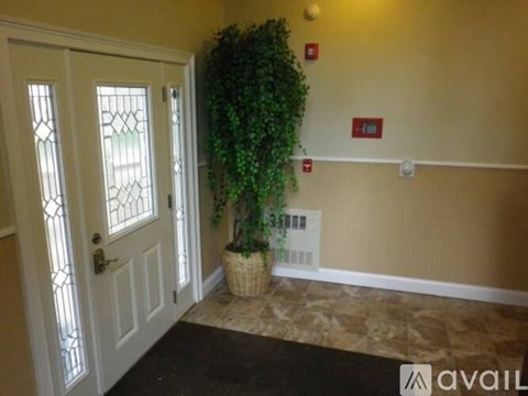 A room with a white door, a plant in a basket and a fire extinguisher on the wall.