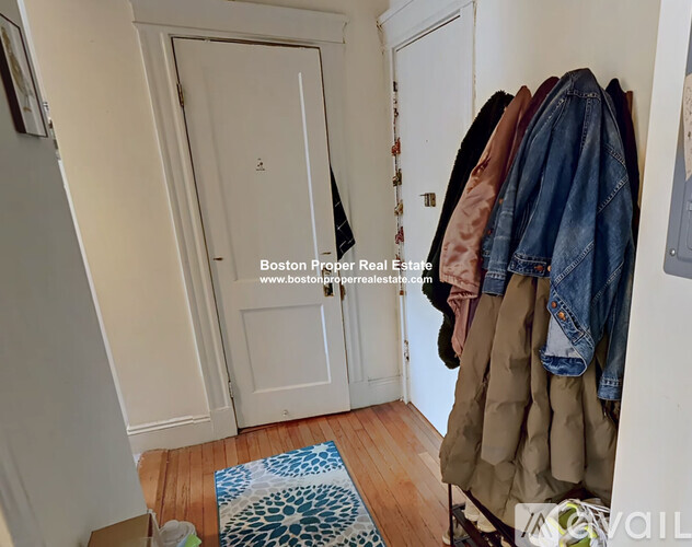 A hallway with a coat rack full of coats and a door on the left.