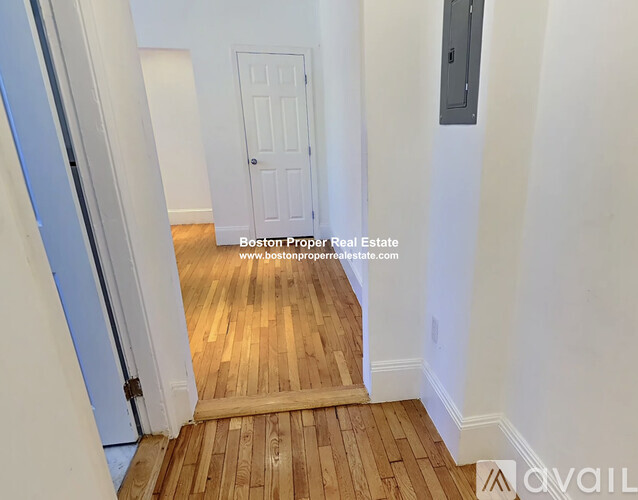 A hallway with wooden floors and white walls leading to a door.