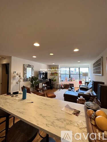 A large kitchen island with a marble countertop is in the foreground of a spacious living room.