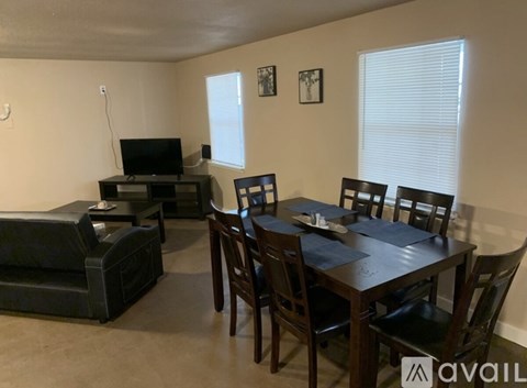 A living room with a black couch, a television, and a dining table with chairs.