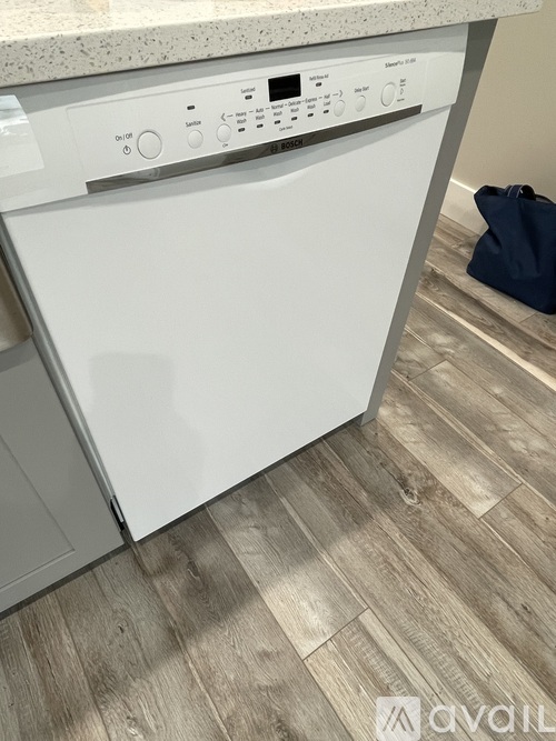 A white dishwasher is in a kitchen with a wooden floor.