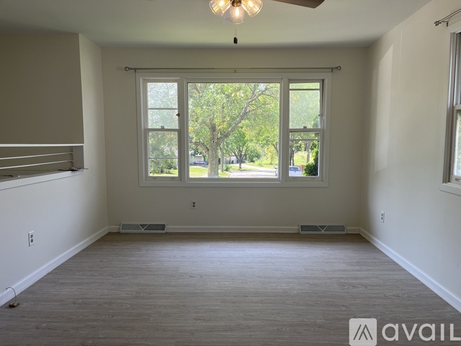 A room with a ceiling fan and a large window with a view of trees.