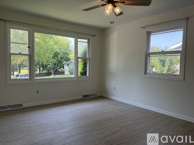 A room with a ceiling fan and two windows.