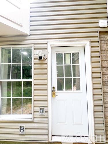 A white door with a window above it and a small camera on the wall.